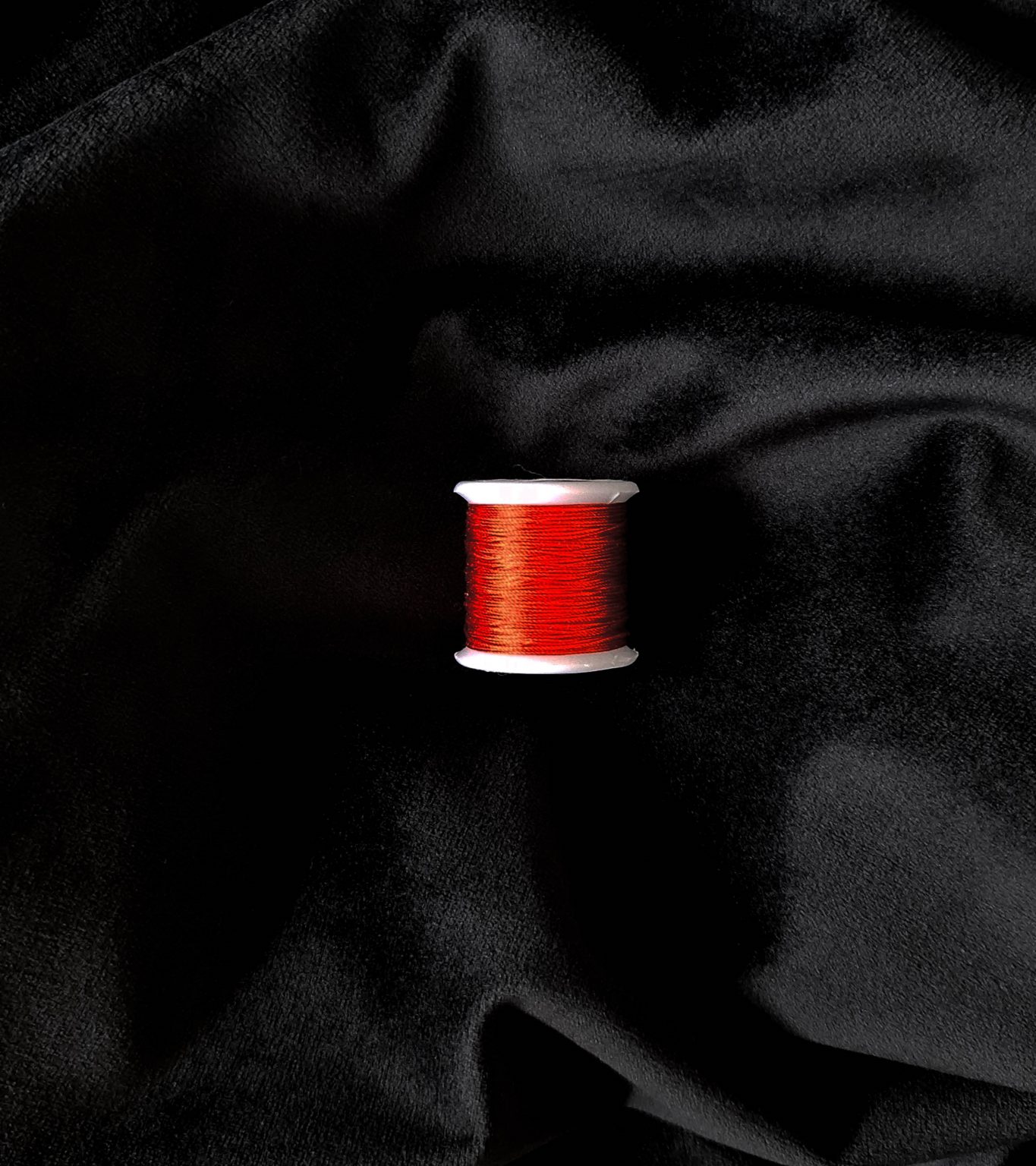 Image of a Chinese red silk spool at the centre of the image, it is laying on top of black velvet.