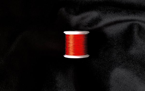 Image of a Chinese red silk spool at the centre of the image, it is laying on top of black velvet.